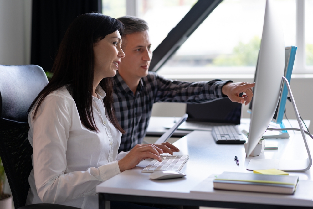 Two colleagues reviewing website security settings together at a desktop computer in a modern office