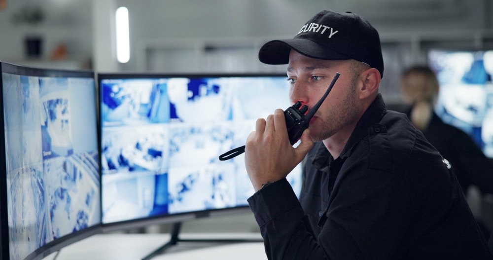 Security guard is looking at computer screens with a walkie talkie in hand - keeping websites safe.