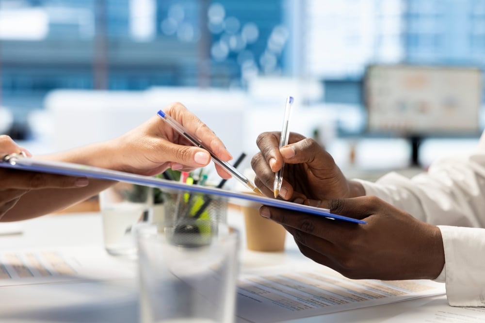 Two professionals exchanging a clipboard document during a vendor review meeting in a modern office